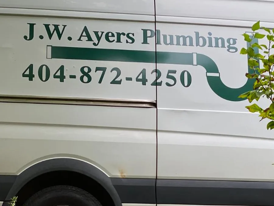 Detail of the J.W. Ayers Plumbing van: the green serif wordmark, the phone number 404-872-4250, and the P-trap drawn as the tail of the lettering.